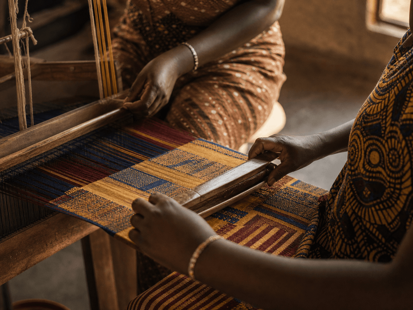 Artisans weaving kente cloth on a wooden loom